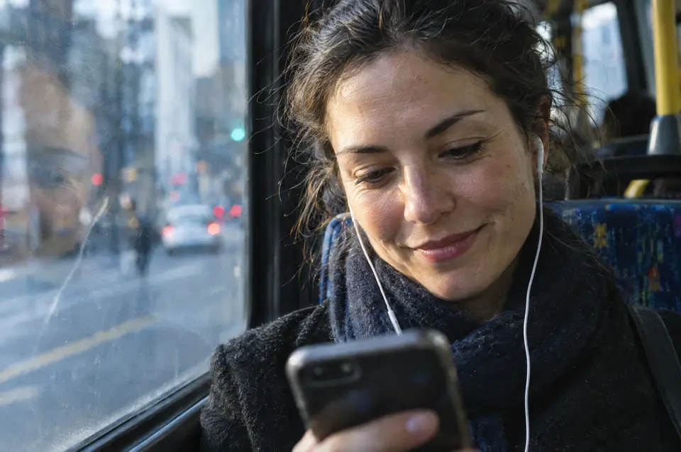 A commuter on a bus smiling while reading an email on her phone